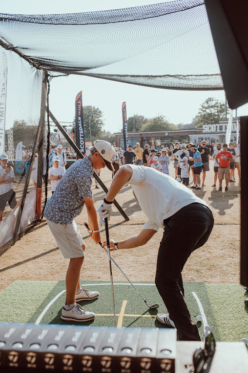 Coach helping a junior golfer in a netted outdoor tech-enabled range bay