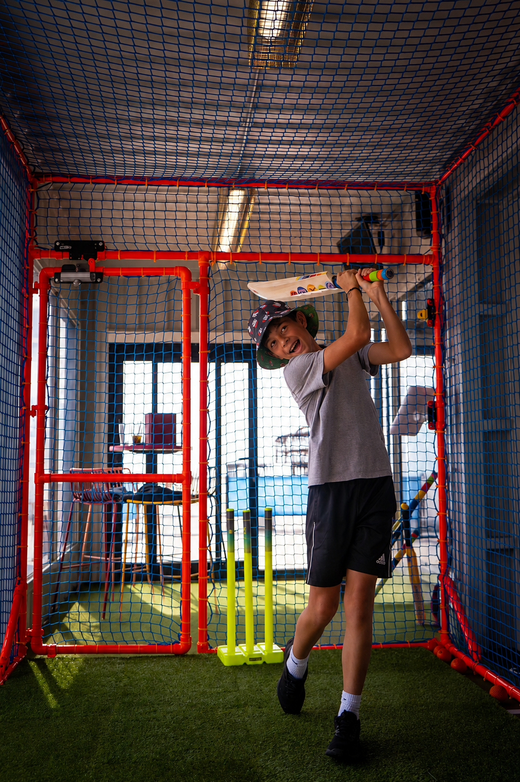 Young batter playing in an indoor netted cricket simulator bay at a hotel
