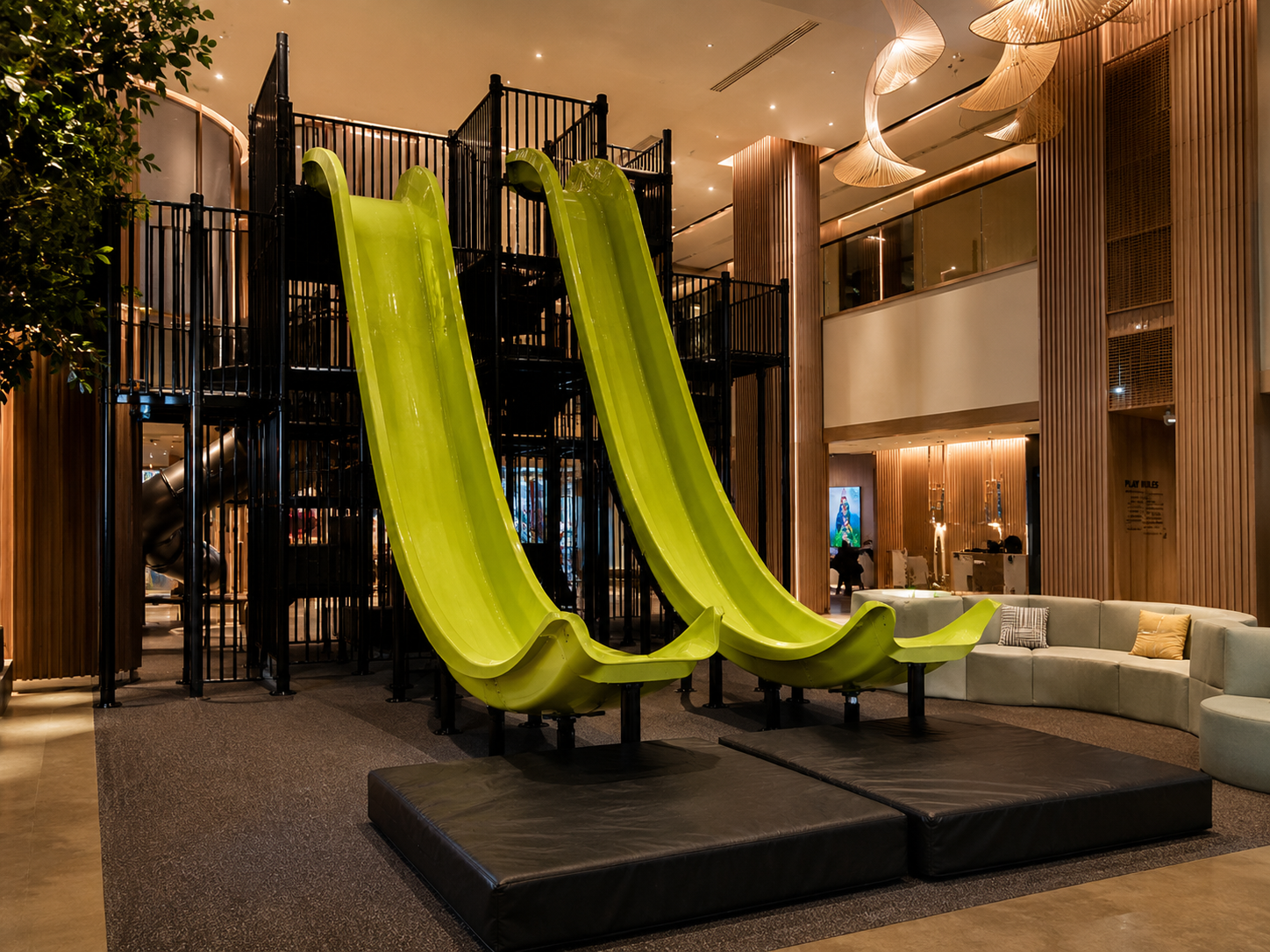 Twin bright green indoor hotel slides and a black play tower in a luxury hotel lobby